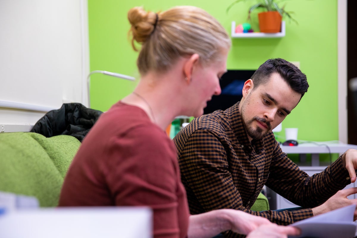 A male graduate student and female professor sit and discuss in a room with lime green walls