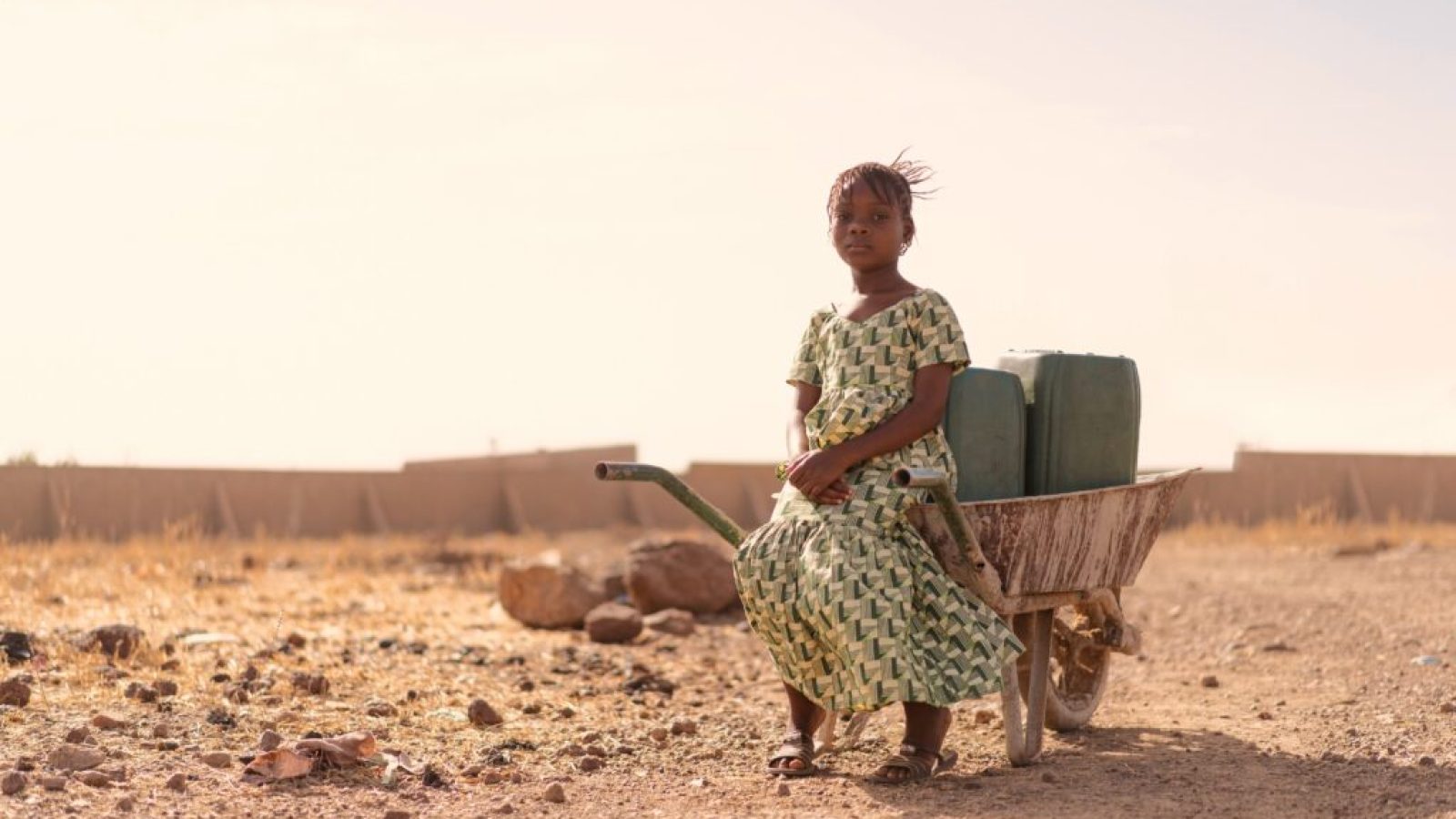 A child sits in a wheelbarrow surrounded by desert landscape.