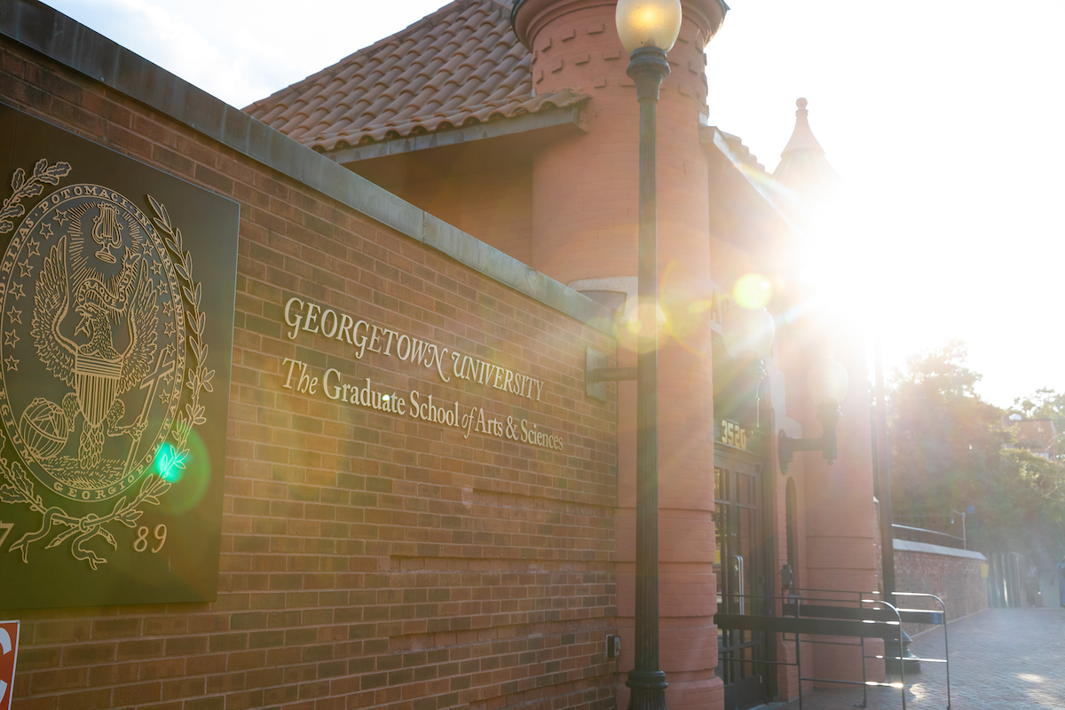 View of Car Barn entrance in the morning with sunlight streaming on the sign with gold letters reading 'Georgetown University, The Graduate School of Arts & Sciences'