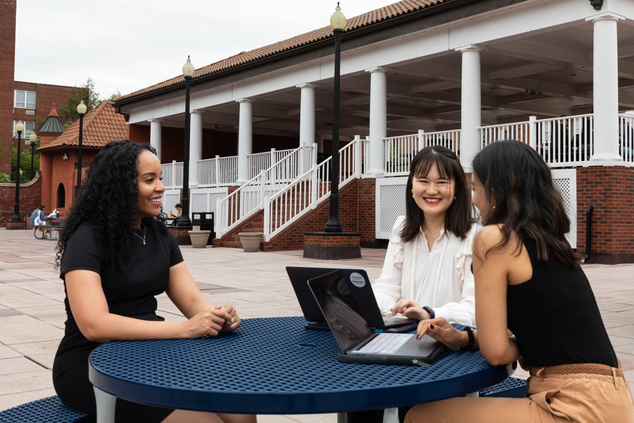 Two graduate students sit at a round picnic table with a faculty mentor