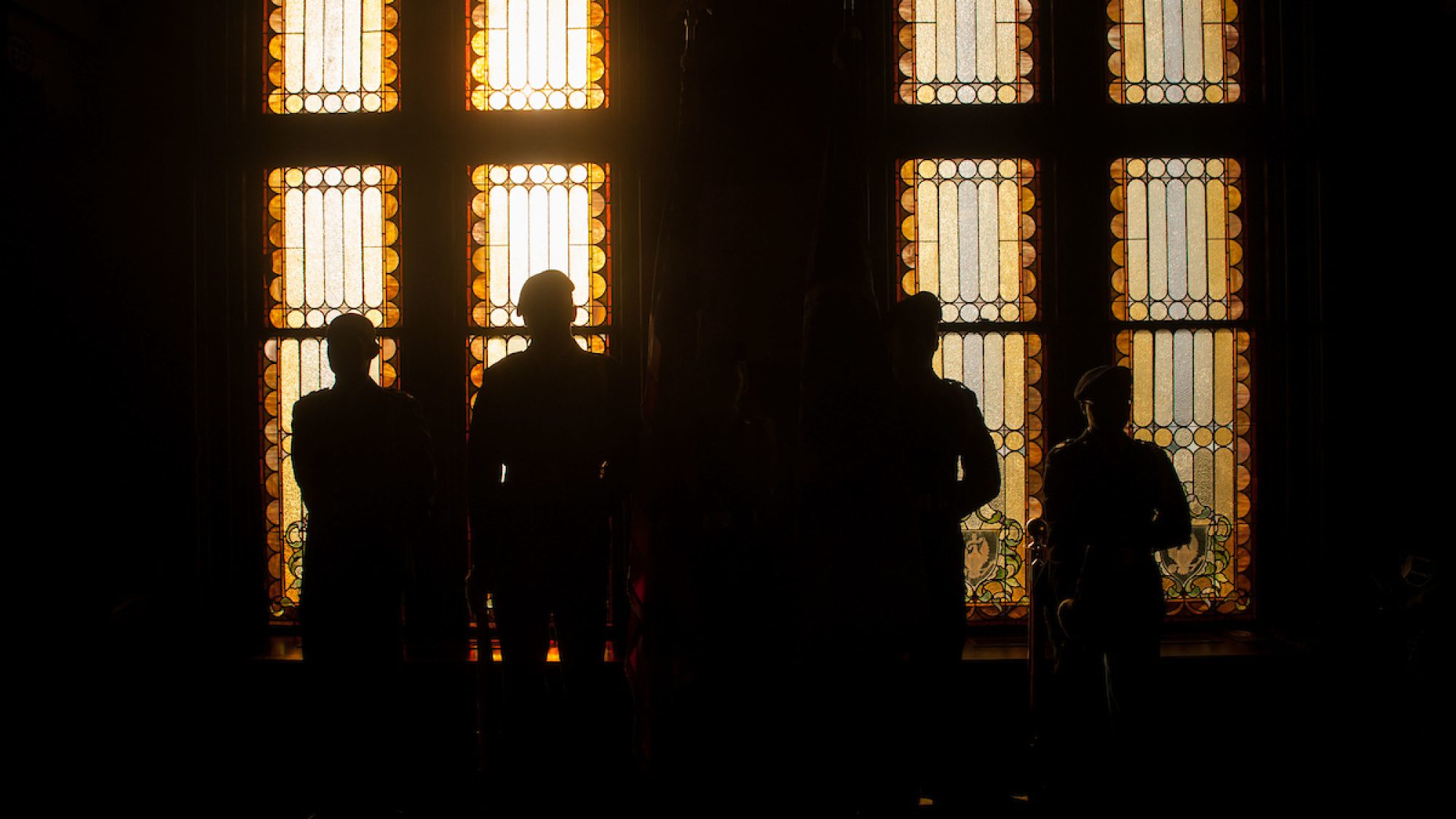 ROTC students in silhouette against light from stain glass windows in Gaston Hall