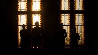 ROTC students in silhouette against light from stain glass windows in Gaston Hall