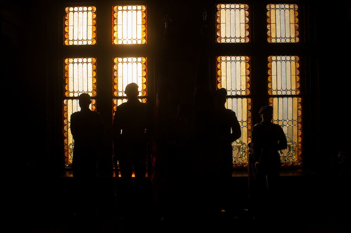 ROTC students in silhouette against light from stain glass windows in Gaston Hall