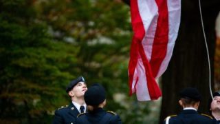 Four ROTC students in uniform look up at an American flag as it is raised onto the flagpole on Copley Lawn at Georgetown University
