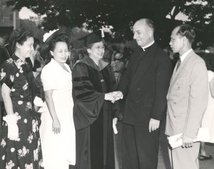 Concepcion Aguila (center) wears a graduation cap and gown next to family and shakes hands with a Jesuit priest