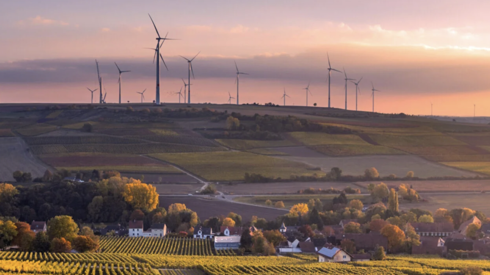 Landscape with green trees, wind turbines and a sunrise over a foothill