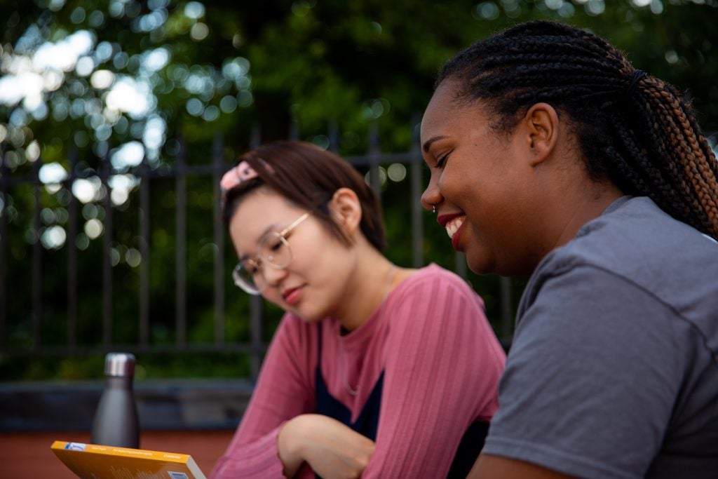 Two female graduate student are sitting at a table outside having a discussion