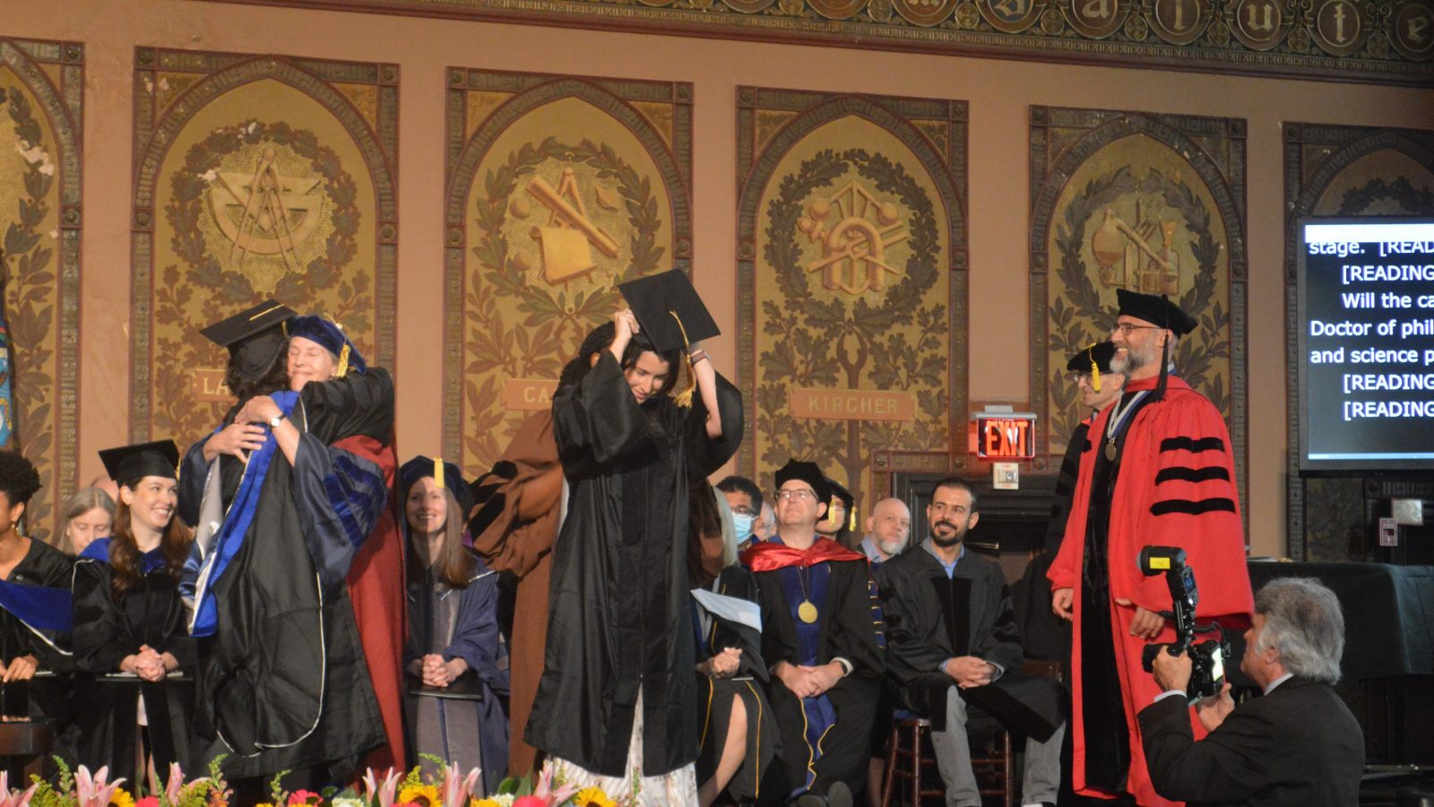 Graduate students on stage getting their doctoral hood placed on their shoulders by faculty