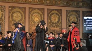 Graduate students on stage getting their doctoral hood placed on their shoulders by faculty
