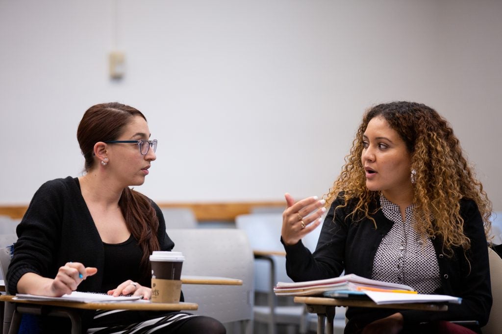 Two students sit at desks in a classroom talking