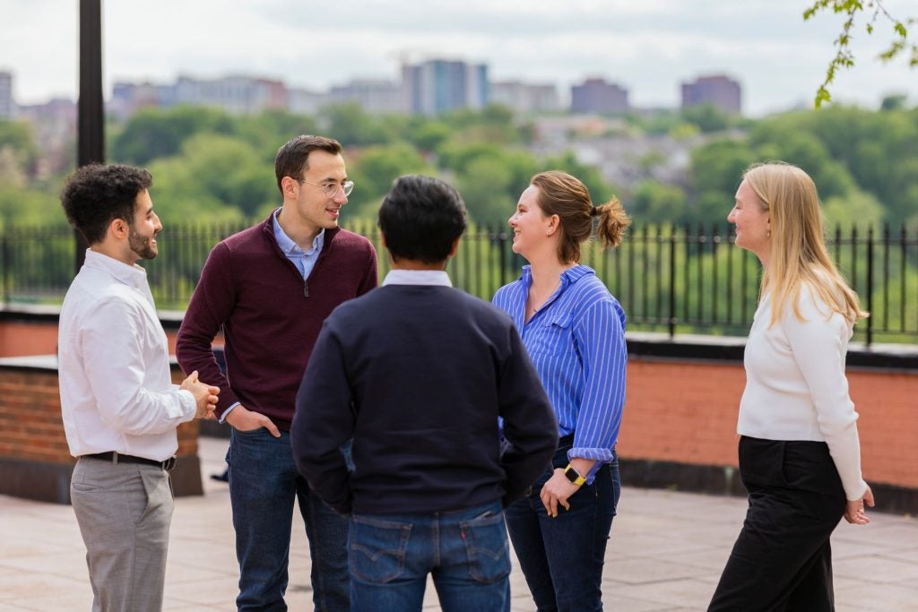 5 graduate students standing together in a circle, talking