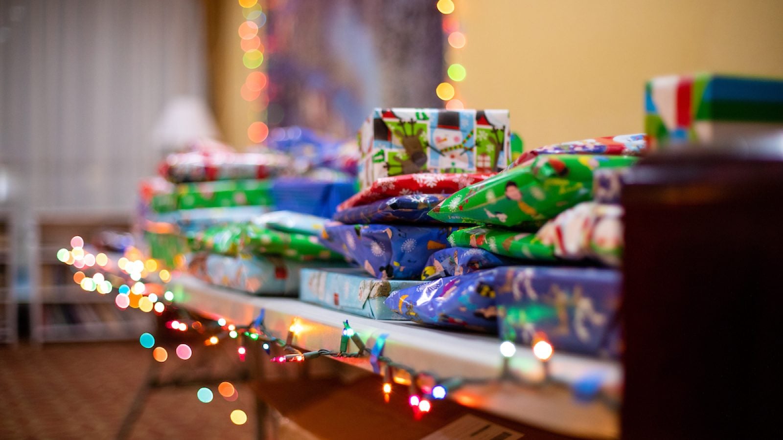 Gifts covered in colorful wrapping paper on top of a table with a string of twinkling lights