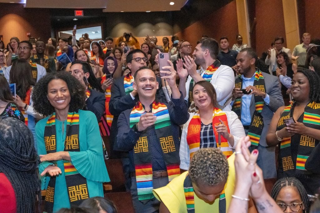 Multiple graduate students – wearing African diaspora, AAPI and Latinx community stoles – cheer and clap at the 2023 Multicultural Graduation Celebration in Lohrfink Auditorium