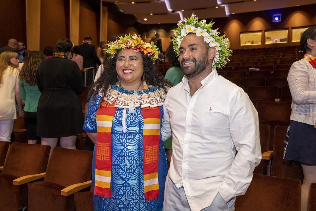 Two graduate students wearing floral headdresses – one of whom is wearing a red, gold and white AAPI community stole – pose for a photo at the Multicultural Graduation Celebration in 2023