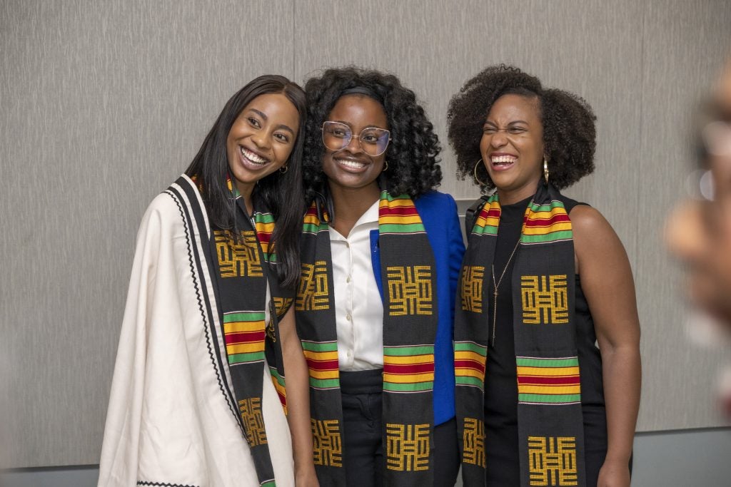 Three graduate students wearing black, gold, green and red African diaspora stoles pose for a photo at the Multicultural Graduation Celebration in 2023