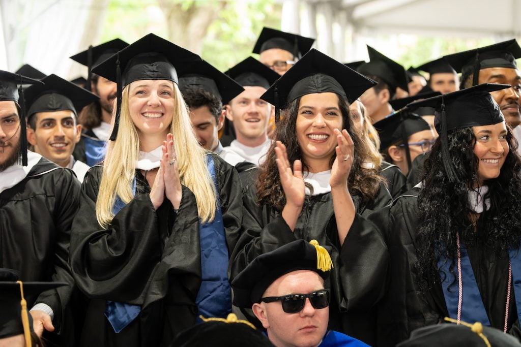 Students wearing graduation robes smile and clap at the Graduate School Commencement Ceremony in 2023