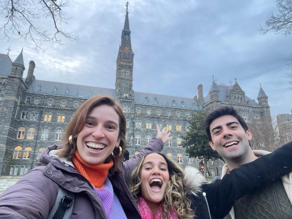 Lucia Szyman Mulero, Carolina Alvarado, Ricardo Pereira Teixeira smile for a selfie with Healy Hall in the background