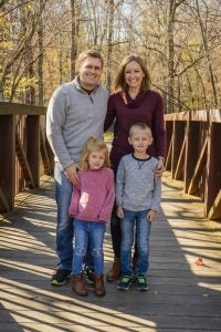 Alison DeBoer and family stand on a bridge with trees covered in yellow leaves in the background