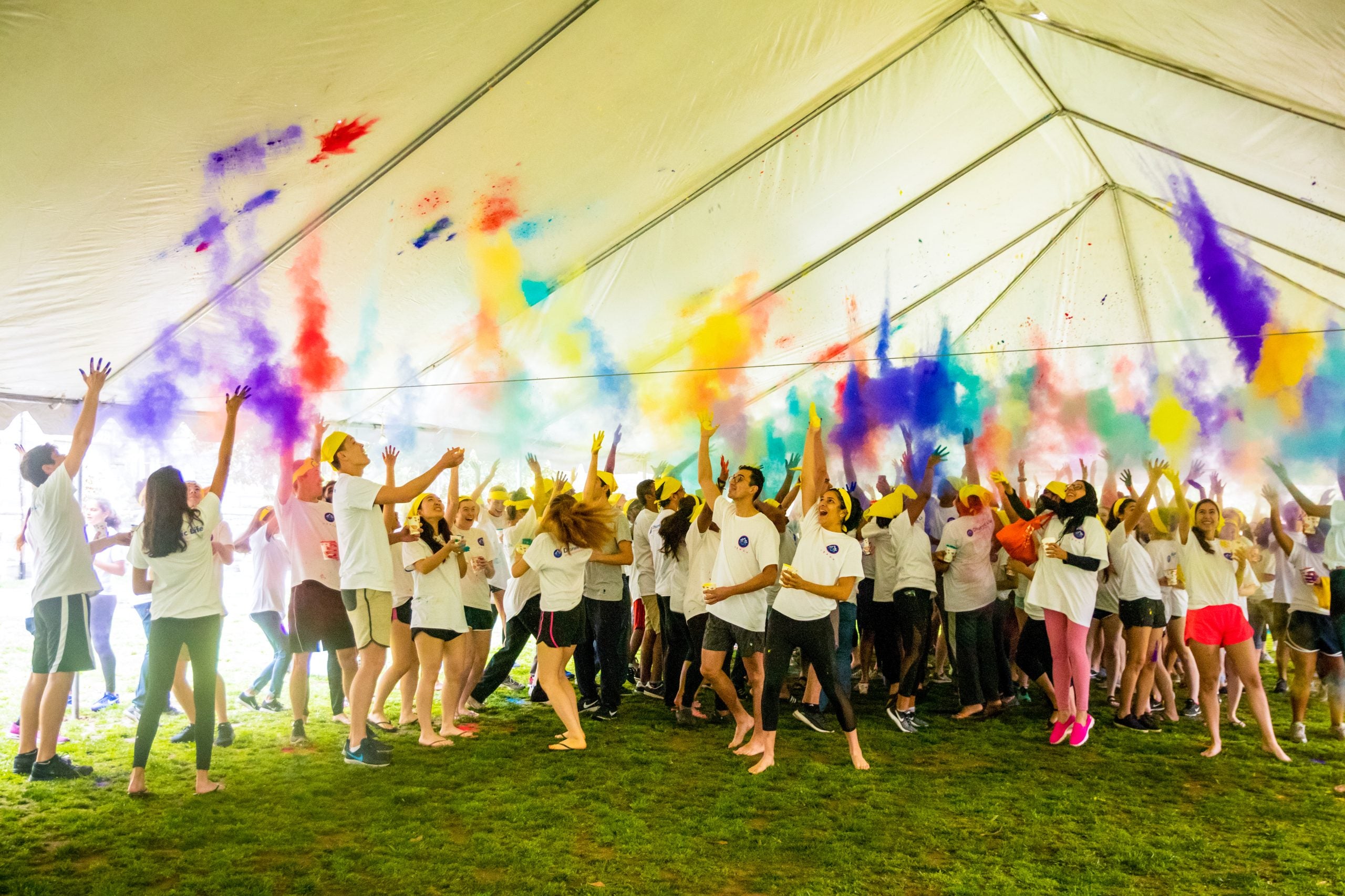 A large group of students throw colored chalk into the air for a Holi celebration on campus