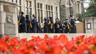 Students wearing black graduation robes line up for the Commencement Ceremony at Georgetown University in May with orange flowers in the foreground