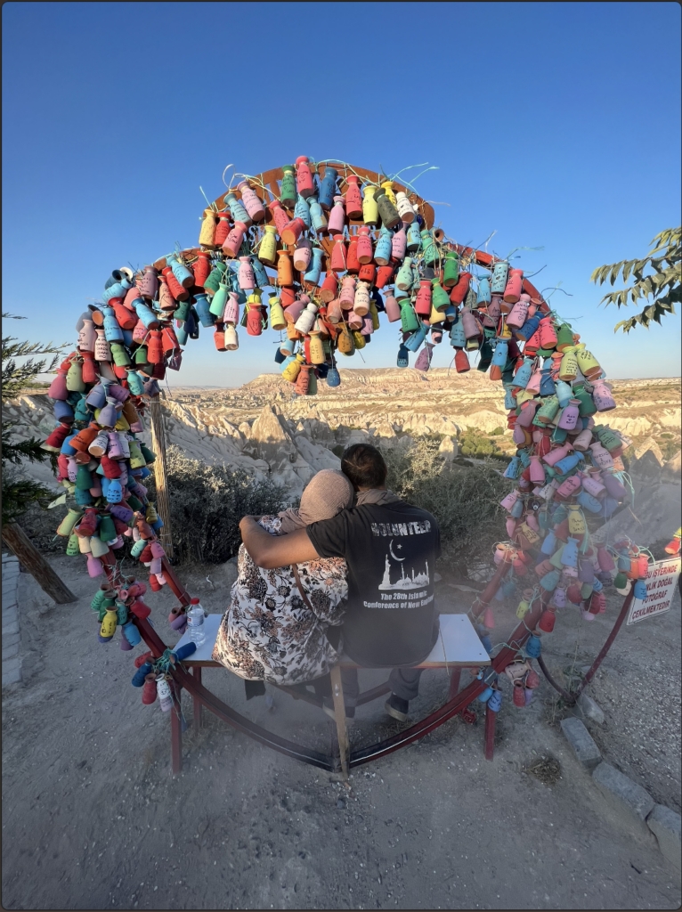 Couple sits on a bench with a colorful archway around them looking out at a desert