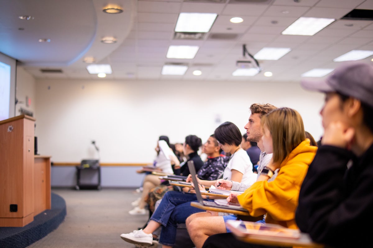 Graduate students sitting at desks with laptops and notebooks attend a class