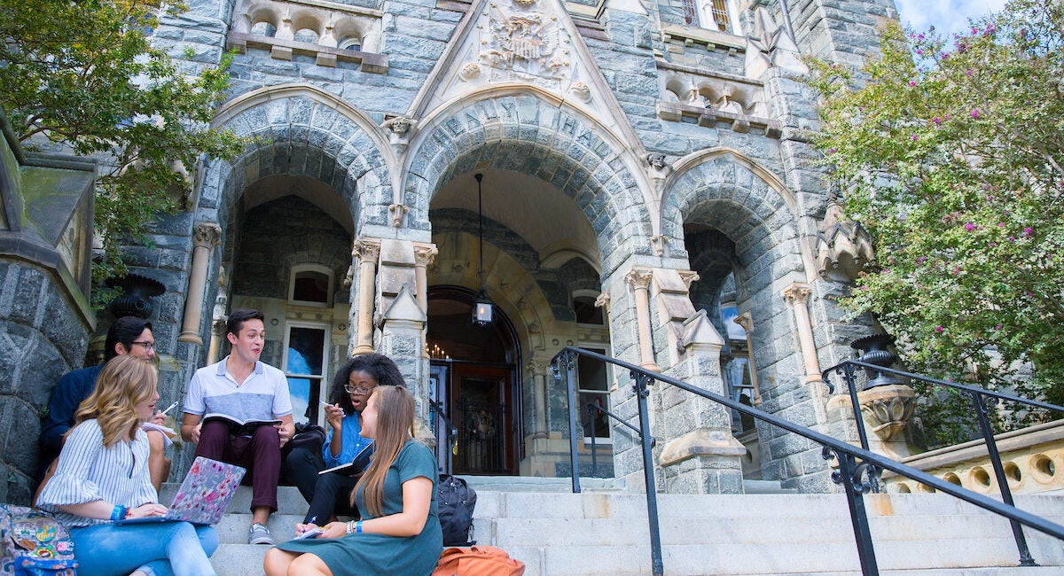 Five students (left) sit outside on the steps of Healy Hall at Georgetown studying