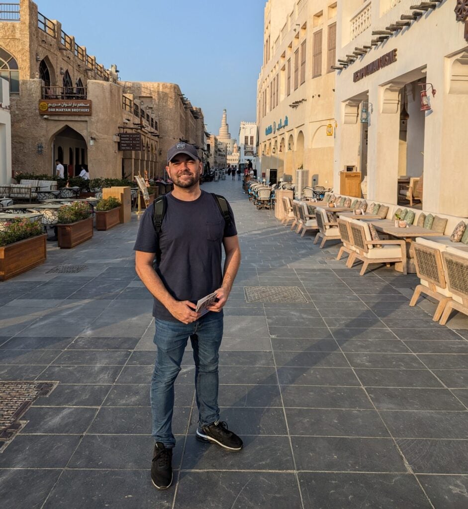 João Sodré (center) stands in the souq (market) in Qatar with stone buildings on both sides of the street and clear blue sky