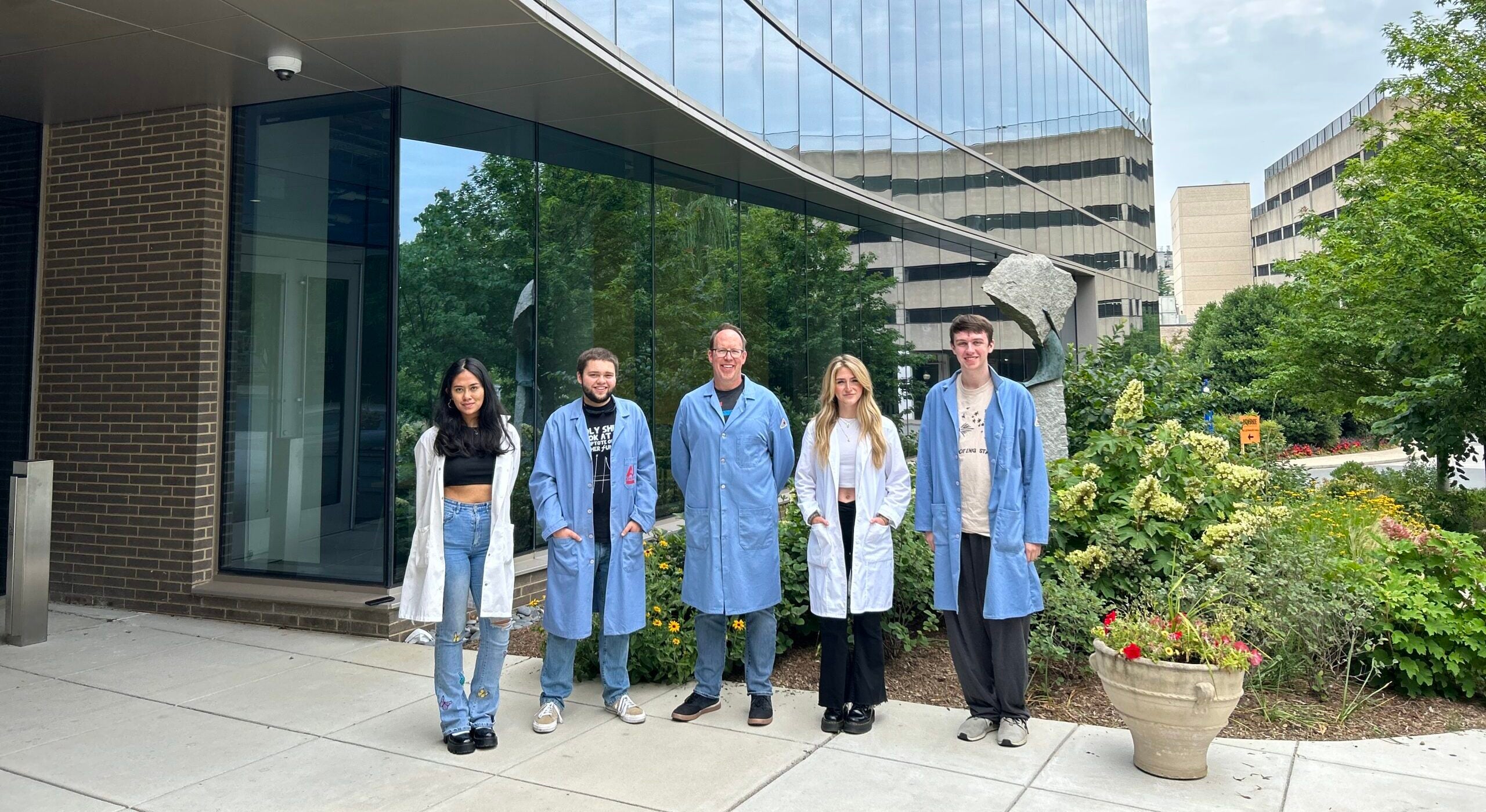 Mary Ruxsarash (left) and peers wearing white or blue lab coats standing outside a building at American University