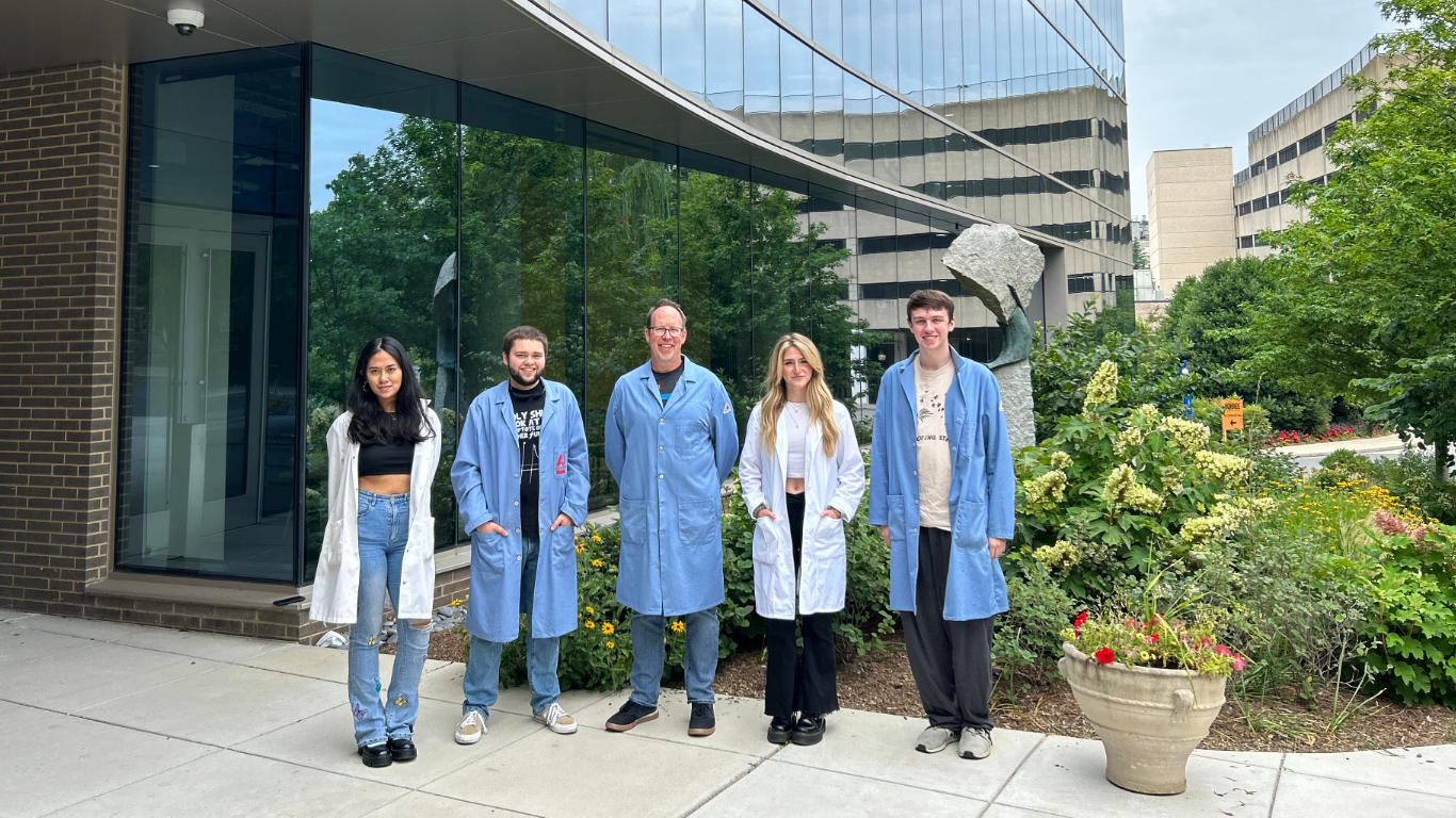 Mary Ruxsarash (left) and peers wearing white or blue lab coats standing outside a building at American University