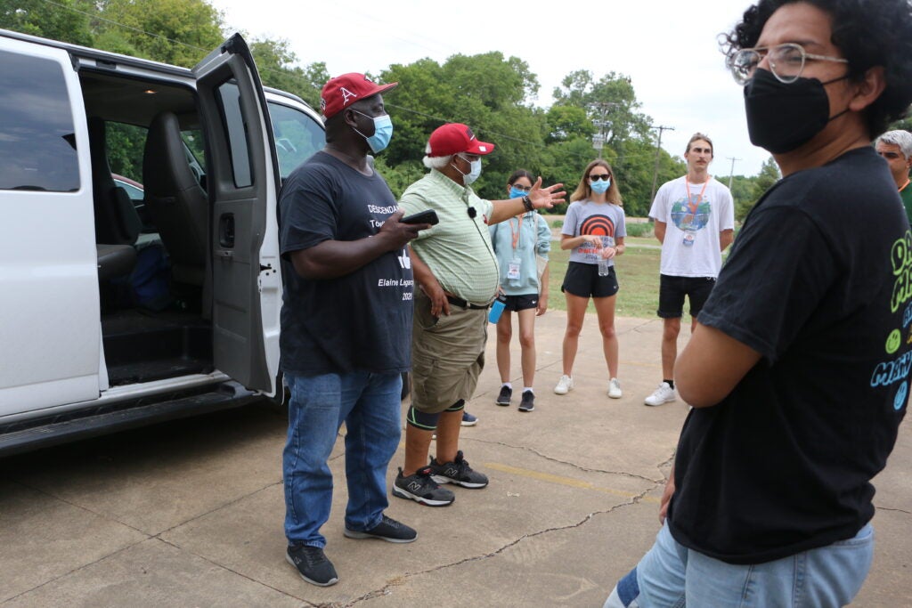 Grey stands (right) wearing a mask with a group of people around a van