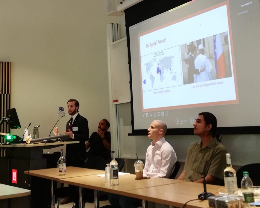 Rodriguez (left) stands at a lectern presenting at a conference with a screen behind him