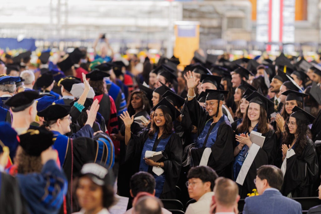 Students, some waving toward friends and family, line up to take their seats at Commencement 2025.