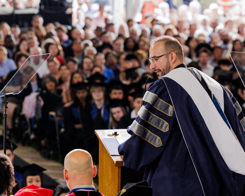 Rev. Luis Arriaga Valenzuela addresses students at the Georgetown Graduate School's 2025 commencement ceremony. He is seen at the podium from behind, looking over his shoulder.