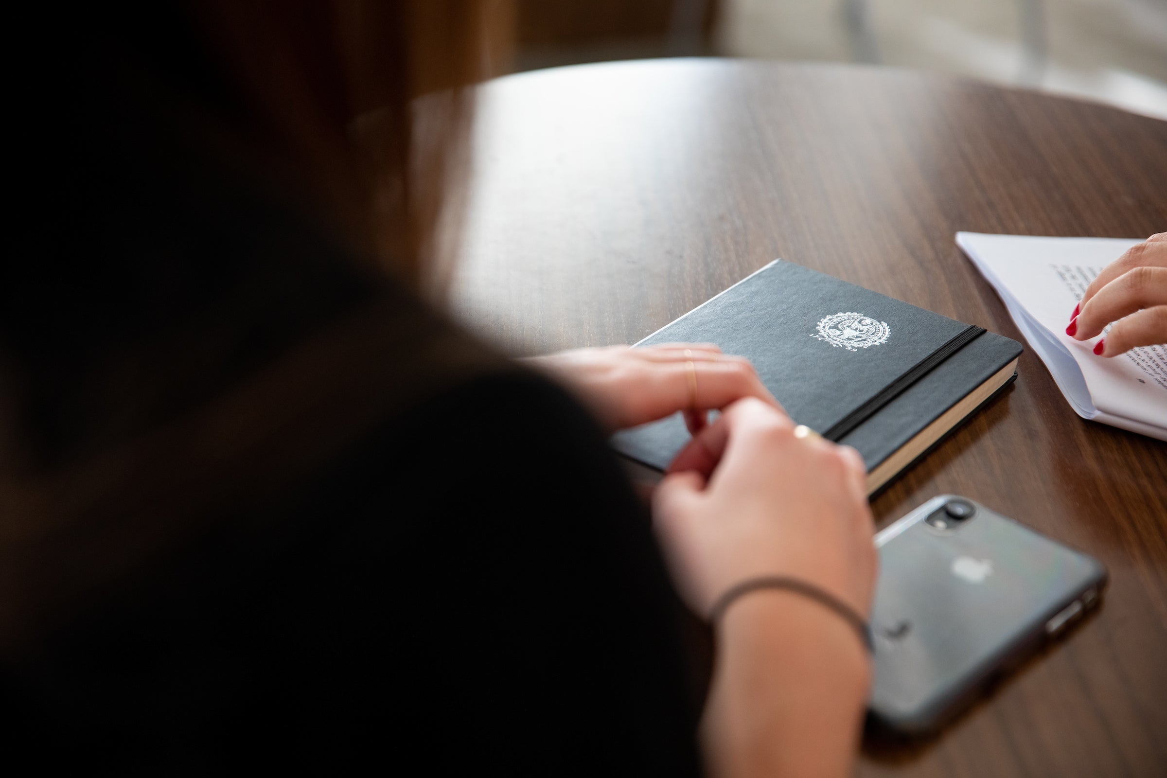 Seen from over her shoulder, a graduate student rests her hand on a notebook with a Georgetown University logo.