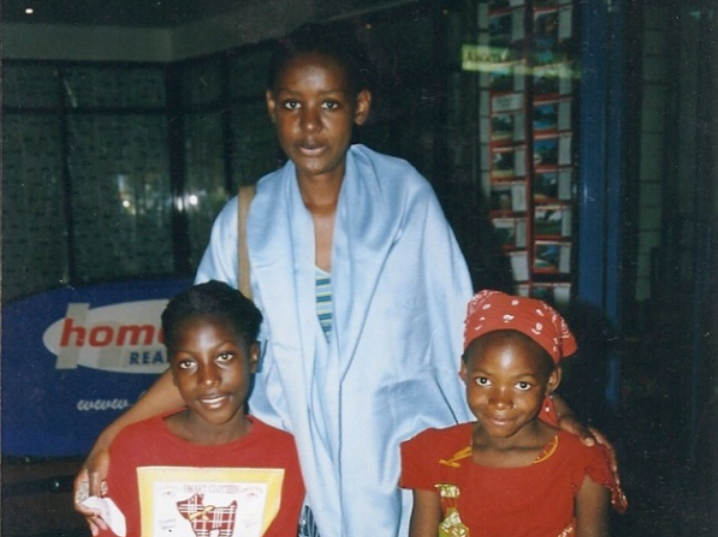 A gaunt and ill Martha Cameron stands in between two Zambian orphan girls, her hands around their shoulders, while doing volunteer work in 2003.