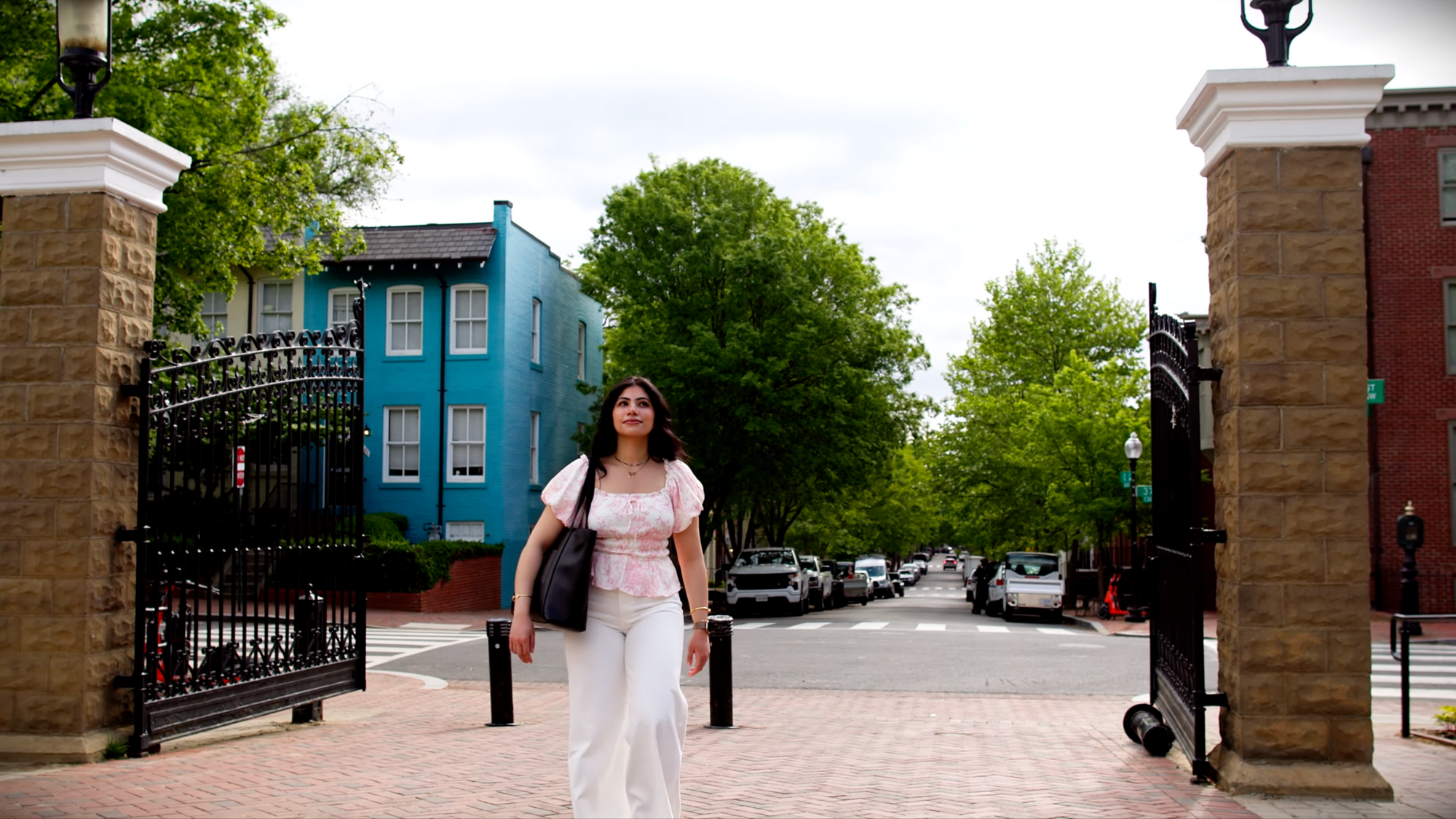 Georgetown alumna Tala Alahmar walks toward the camera and through the front gates of Georgetown University.