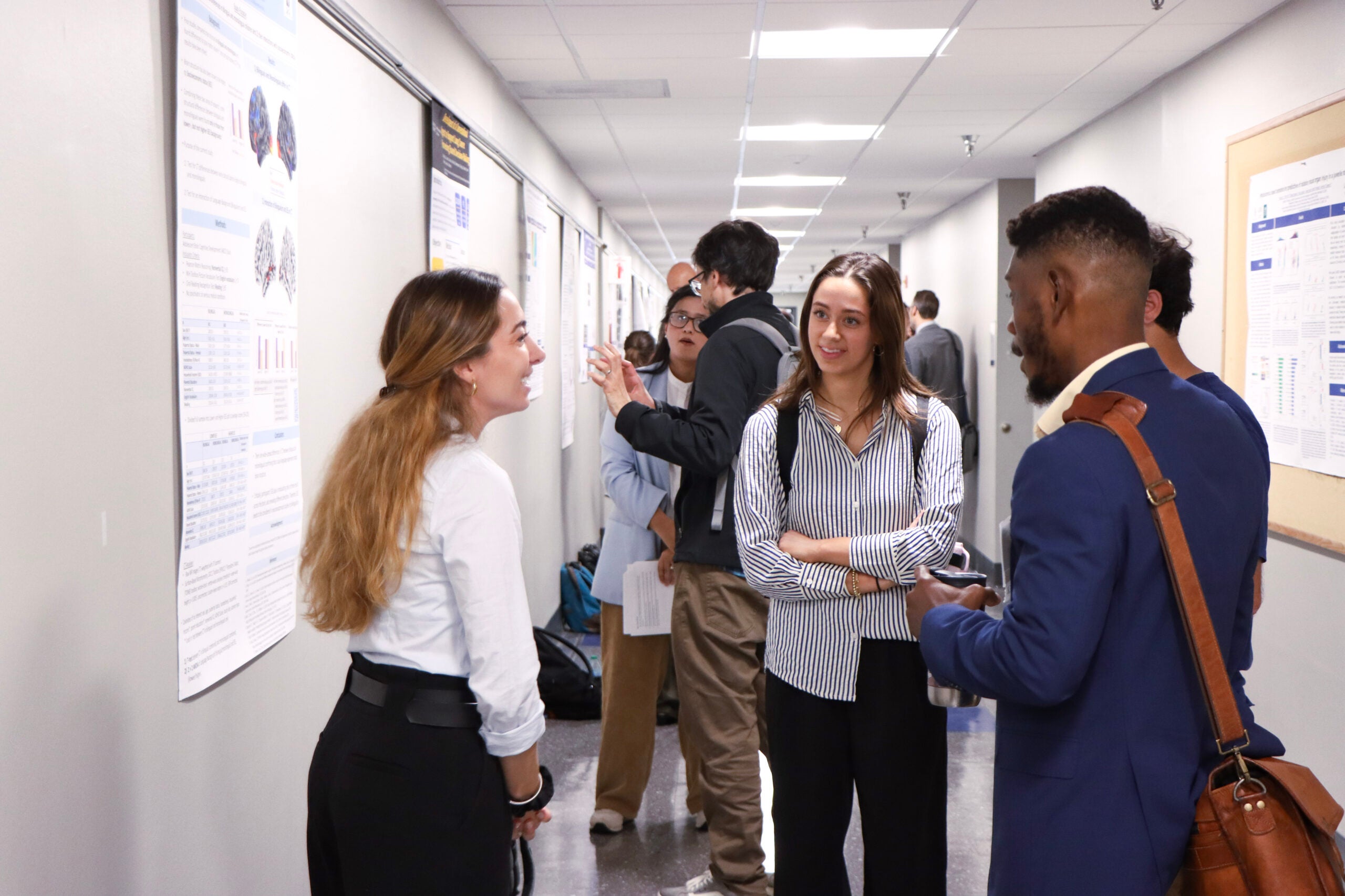 A grad student presents a poster at Student Research Day while two other students listen attentively.