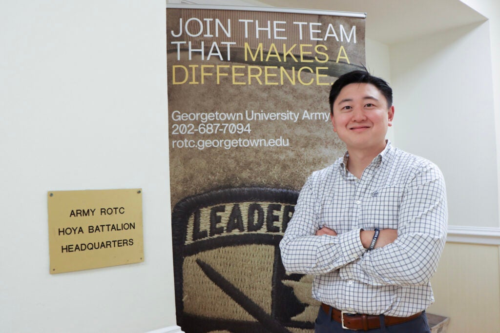 Yu stands, arms crossed, in front of the Army ROTC Hoya Battalion Headquarters sign.