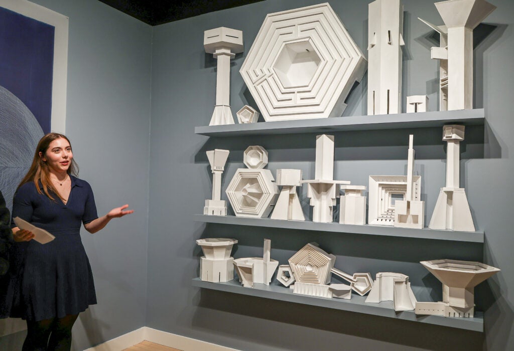 A student presents in front of the "Inventory 1" sculpture by Kendall Buster.