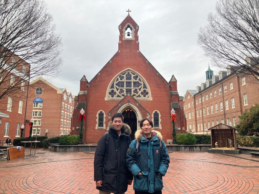 Mideum Hong, right, stands next to Haweon Lee in front of Dahlgren Chapel. Both men are wearing winter coats and the chapel is decorated for Christmas.