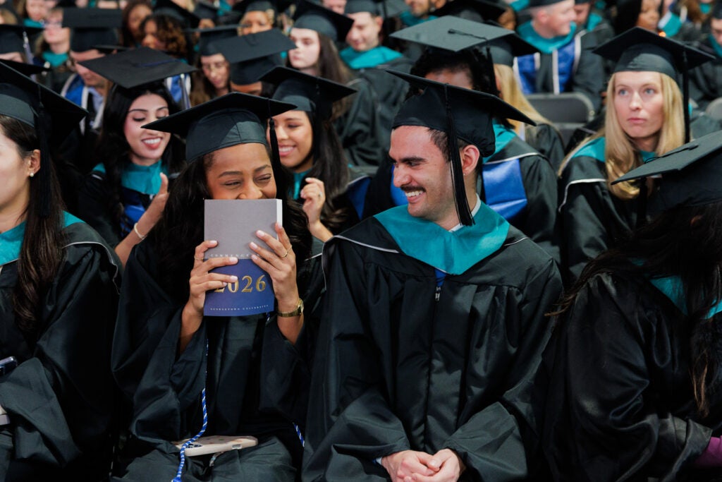 Two master's graduates share a giggle in a sea of graduating students.