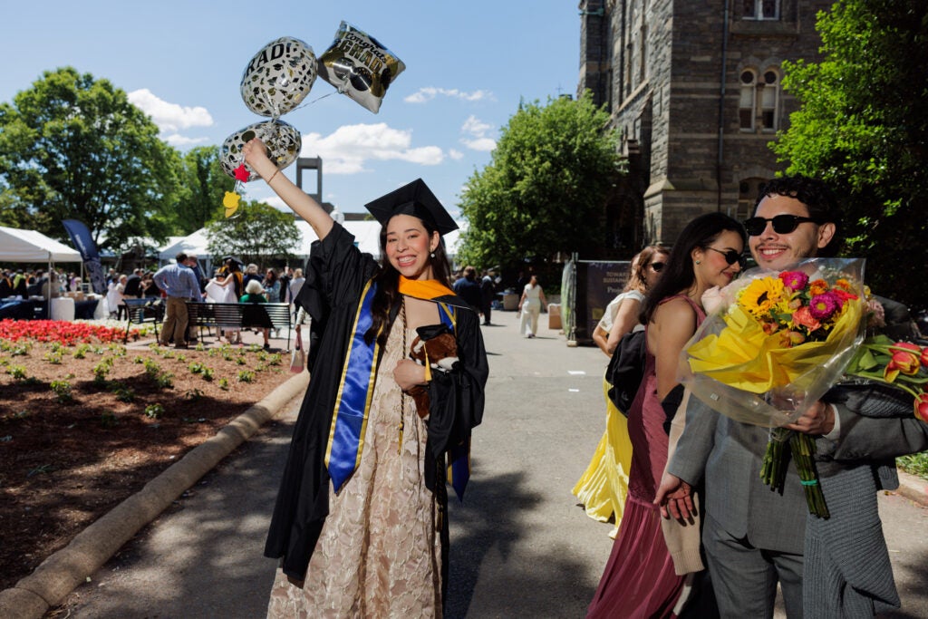 A master's graduate grins and holds a bundle of balloons above her head.
