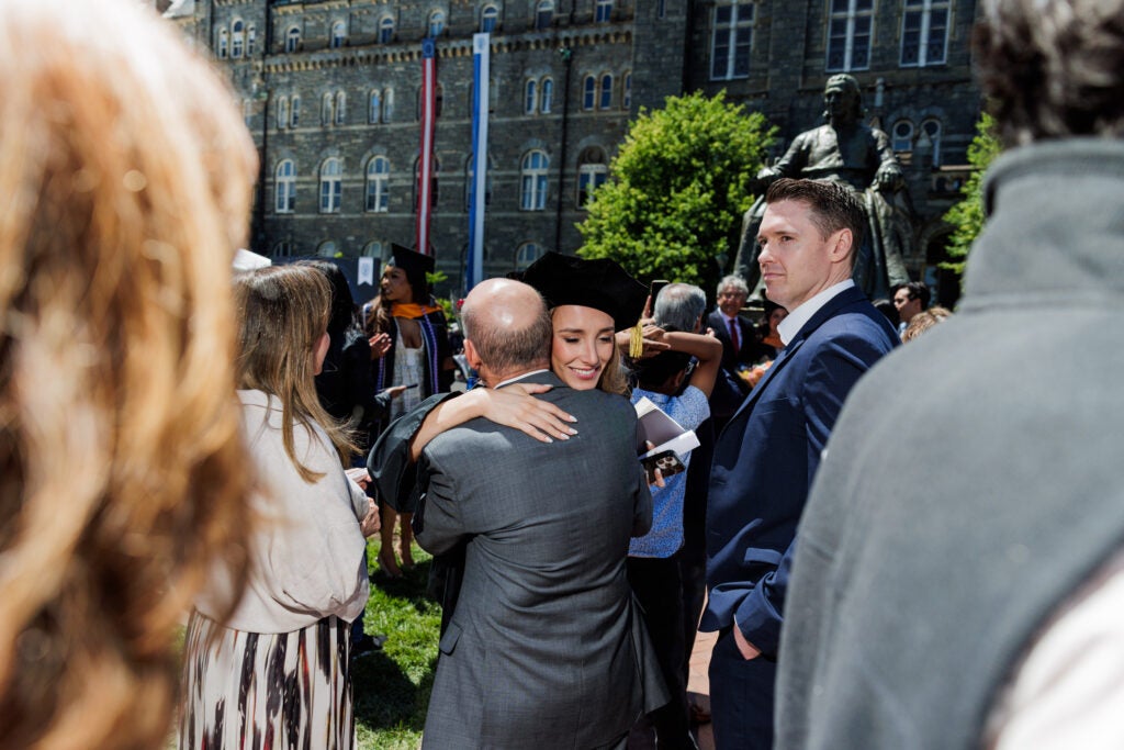 A graduating Ph.D. student smiles and hugs a loved one on the Healy Lawn.