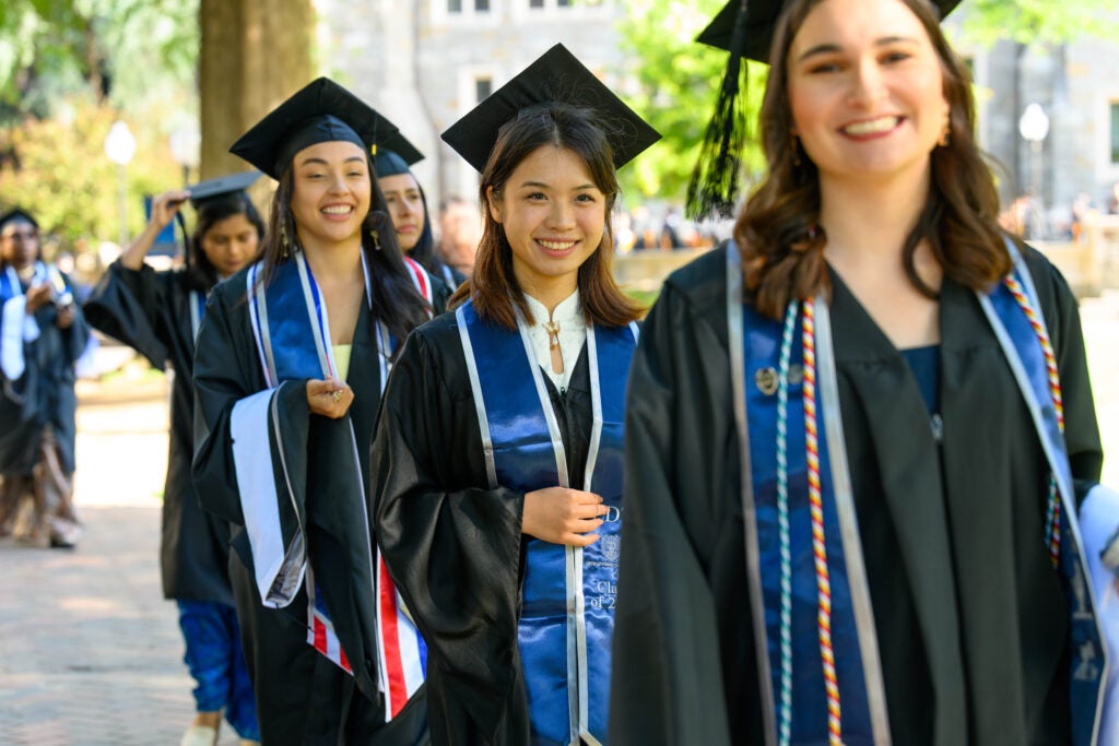 A group of female master's students smile as they walk into Commencement.