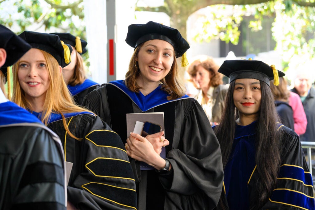 A female Ph.D. graduate smiles and peers ahead at the processional line into the Commencement ceremony.