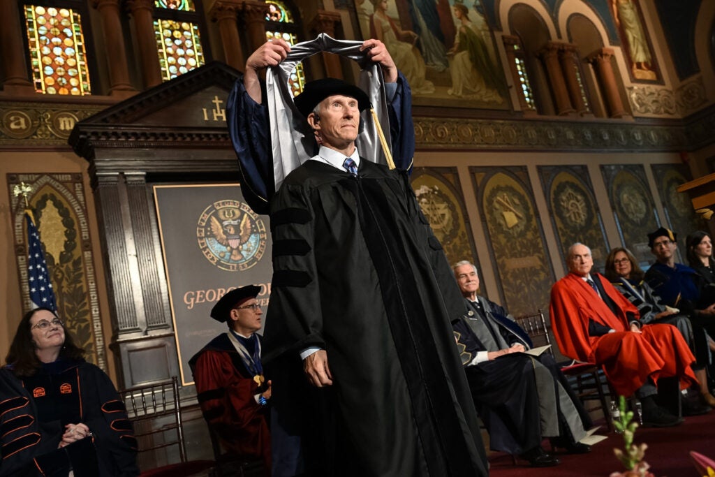 A male Ph.D. graduate receives his doctoral hood from his mentor.