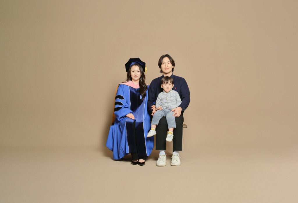 Mideum Hong is pictured with his wife and child, photographed against a beige photo studio background.