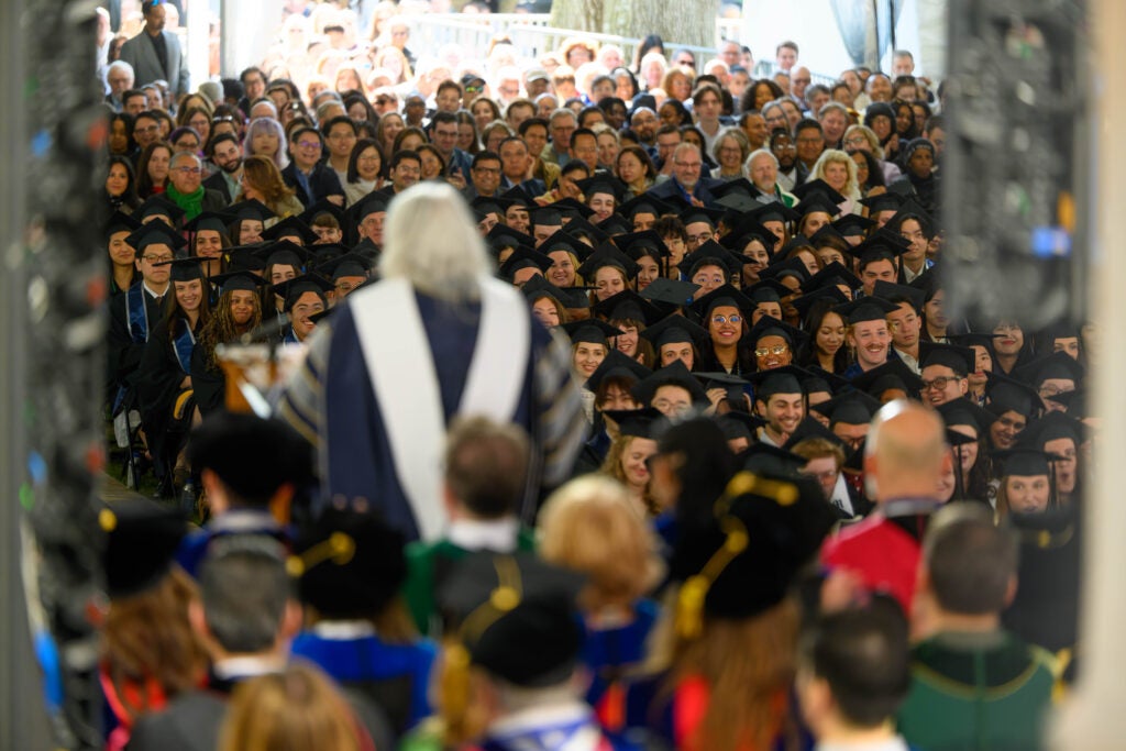 Mary Beard, seen from behind, gives a speech to a crowd of graduate students and their families.
