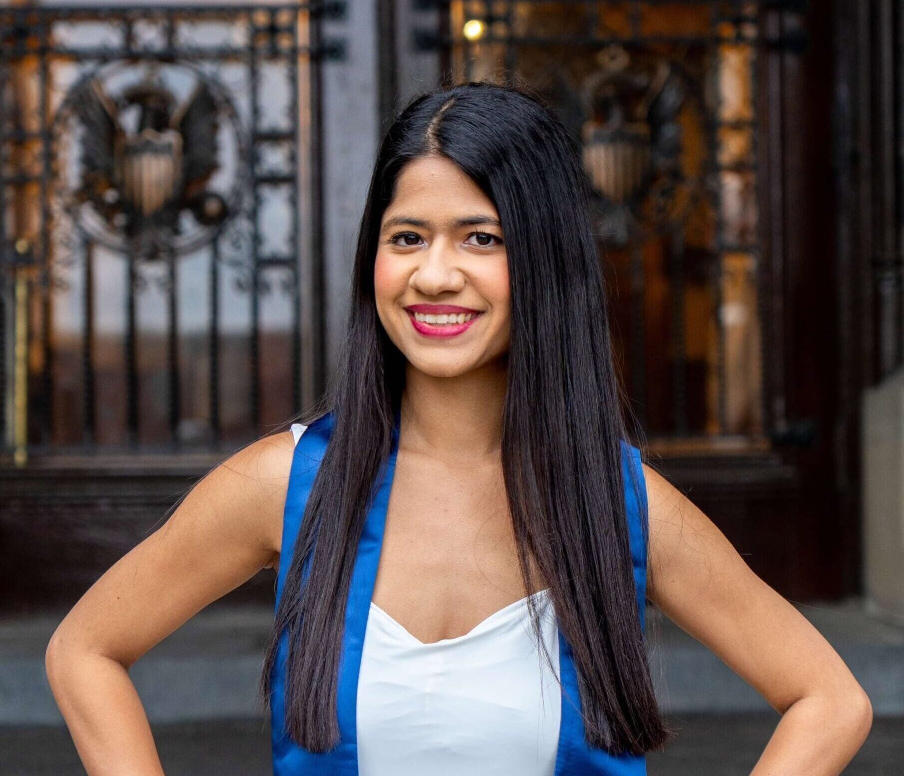 Master's student Priyasha Chakravarti wears a graduation sash in front of the doors to Healy Hall.